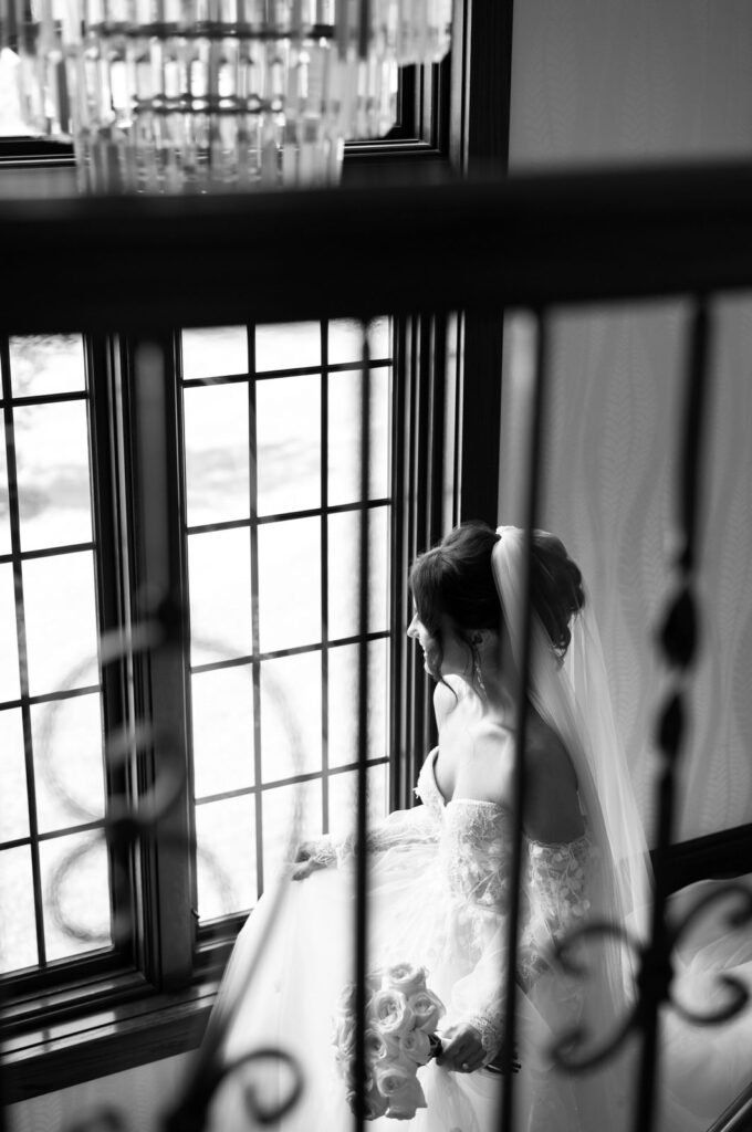 bride walking down the staircase of Venue3Two while looking outside the window on her wedding day