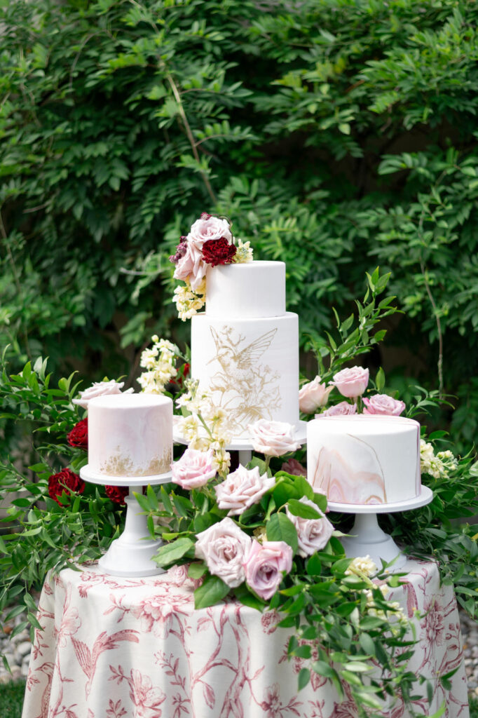 3 cakes surrounded by pink flowers and greenery crafted by Sweet Details GR