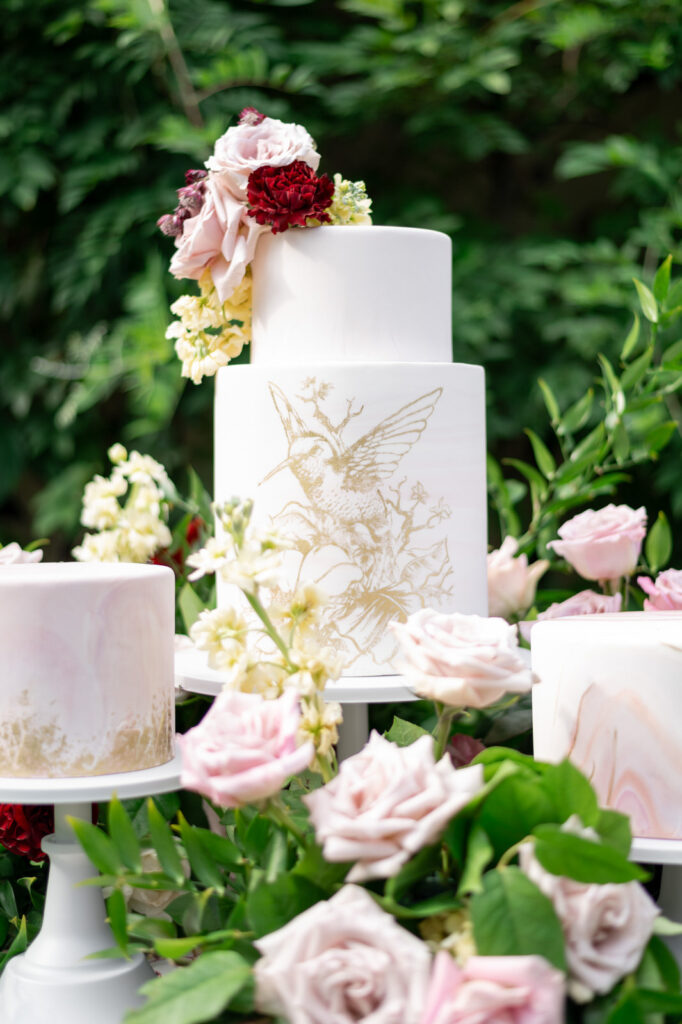 a white two tier wedding cake with a golden hummingbird painted on it