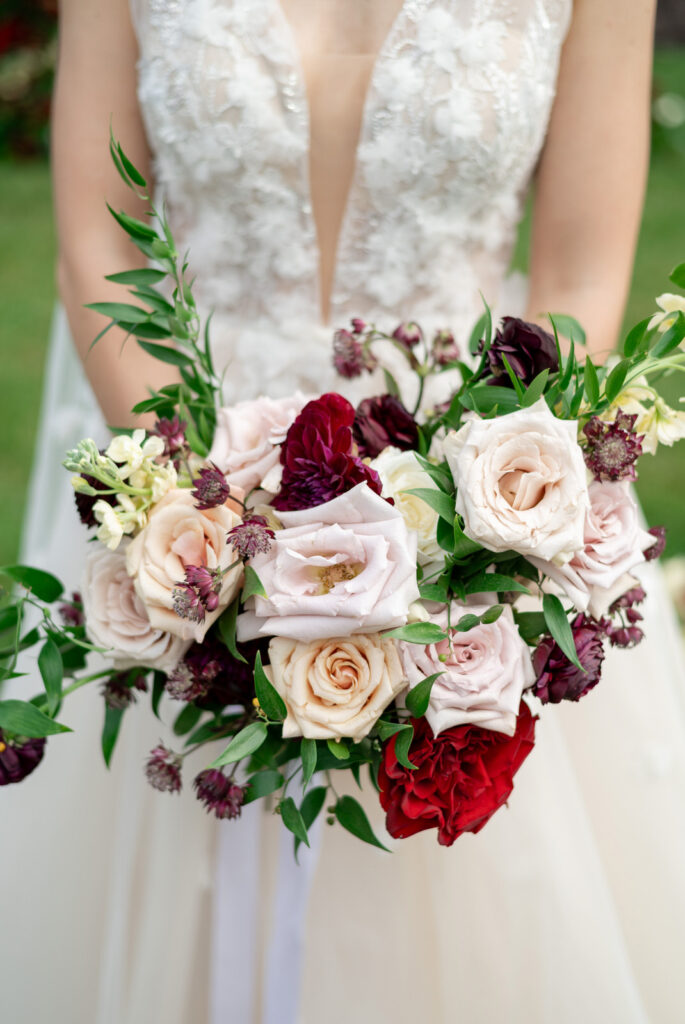 a fall inspired wedding bouquet made up of white, pink, and red harden roses and greenery