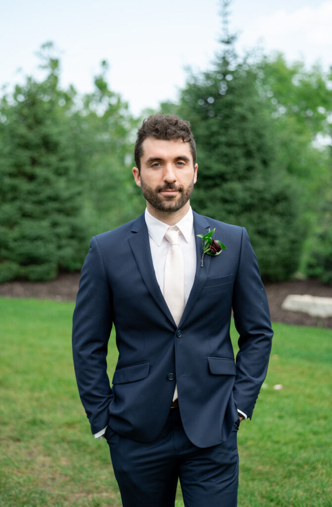groom in a navy suite with a white tie walking with pine trees in the background