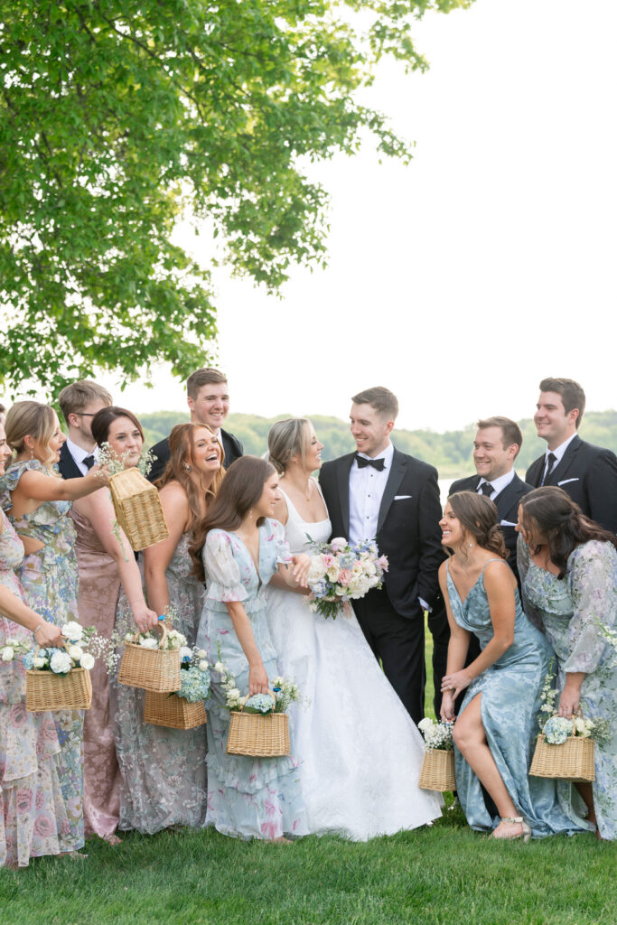 bride and groom surrounded by their bridal party in various pastel colored bridesmaid dresses and black tuxes