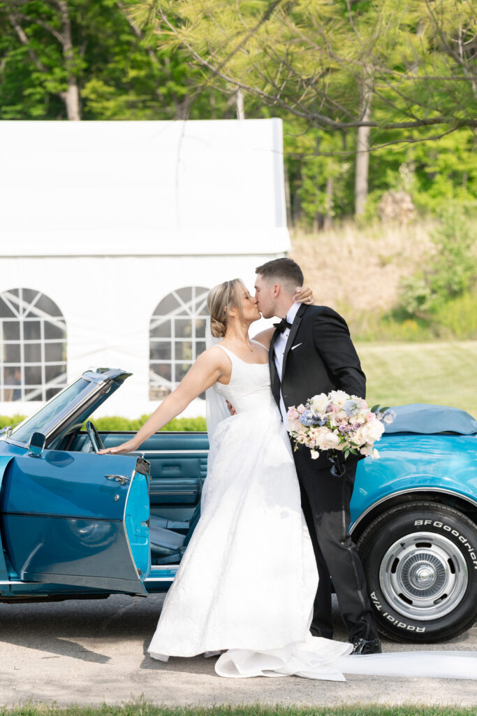 bride and groom kiss in front of a vintage blue Chevy Camaro at their Waldenwoods Wedding
