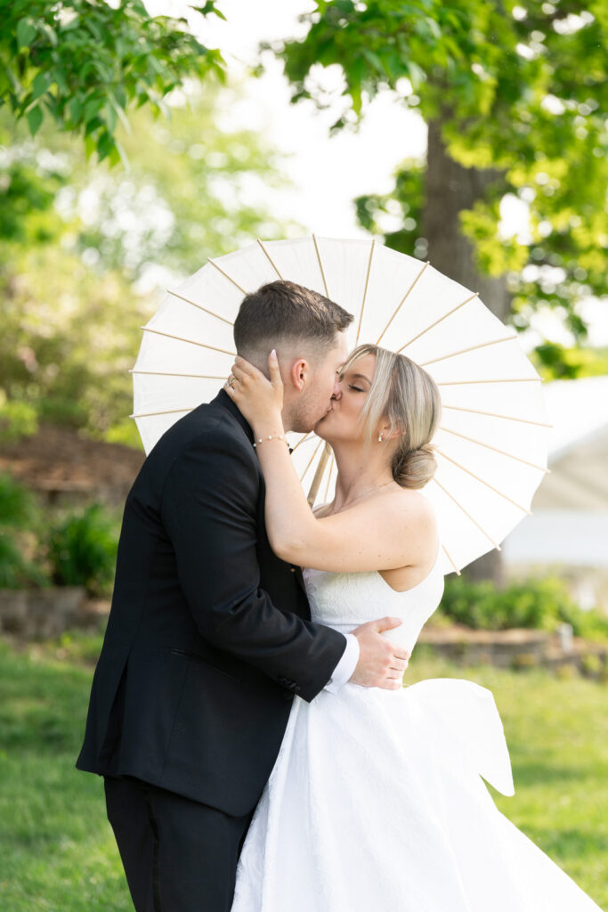 Mariah and Josh share a kiss under a white paper parasol at their Waldenwoods wedding at sunset