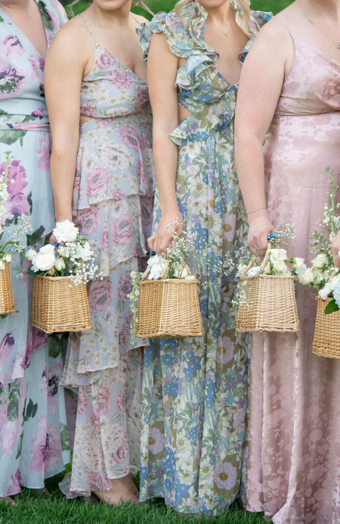 bridesmaid dresses with various patterns and pastel color pallet as they're holding whicker baskets full of flowers