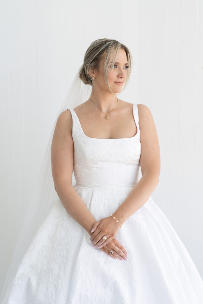 classic bride wearing a floral textured wedding dress, crossing her hands and looking out into the distance