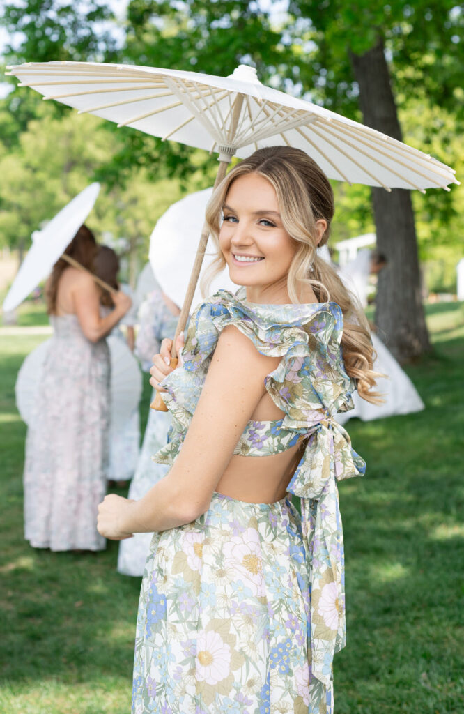 bridesmaid in colorful and patterned dress holding a white paper parasol smiling over her shoulder