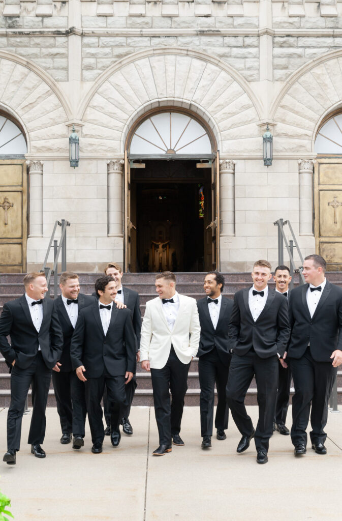 groom and his groomsmen walking and laughing in front of the steps of Basilica of St. Adalbert