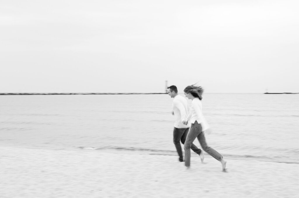 couple running hand in hand in the sand during their Muskegon engagement photo session