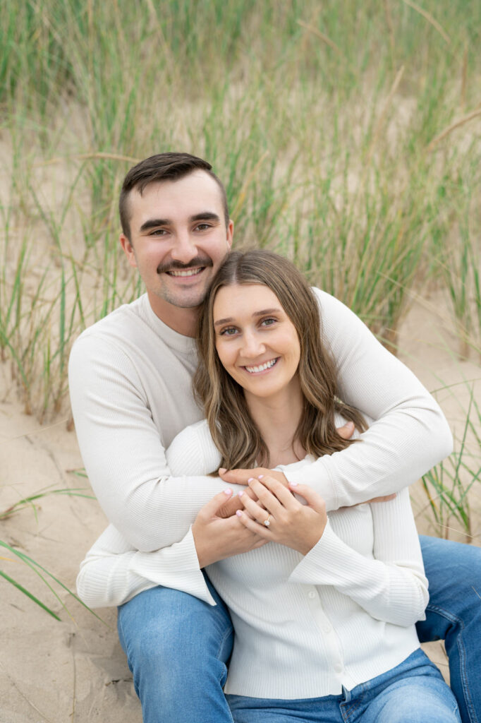 Becca and Alex cuddling and sitting on the sand dunes during their Muskegon engagement session
