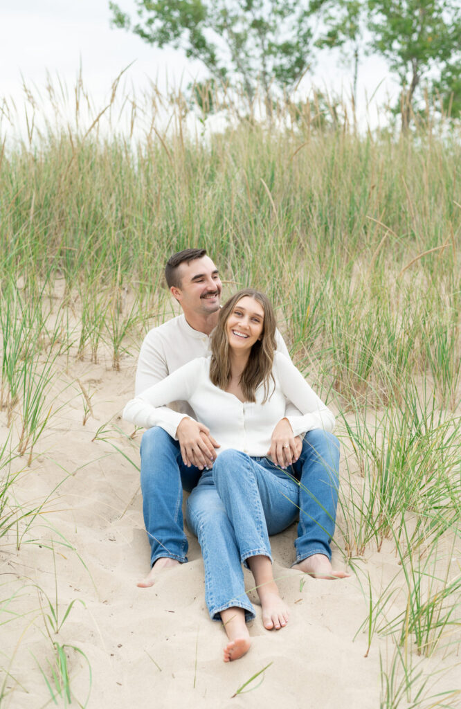 engaged man and woman sitting on the sand dune hills on Lake Michigan during their engagement session