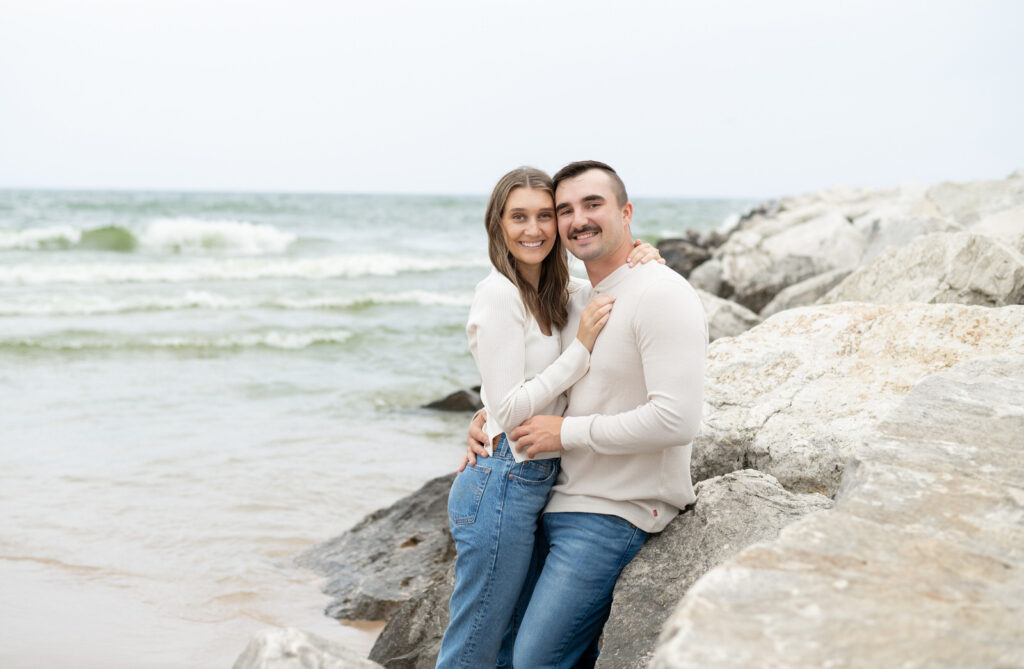 man and woman chest to chest smiling against huge beach rocks in Muskegon