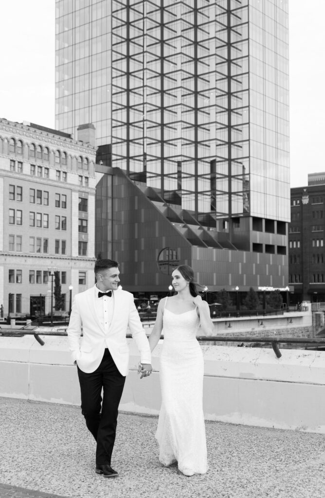 bride and groom holding hands and walking on a bride over the Grand River in downtown Grand Rapids