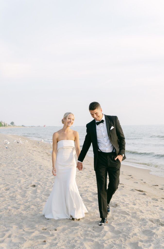 bride and groom walking hand in hand at sunset on the shore of Lake Michigan after their Holland Michigan wedding