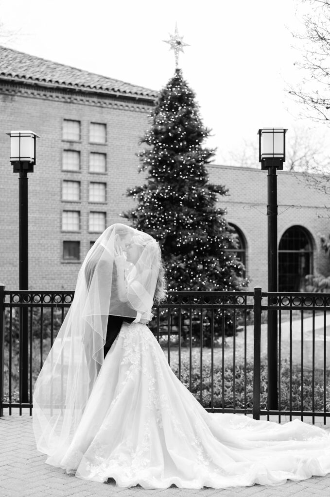 bride and groom snuggling under the veil outside in front of a Christmas tree at Saint John's Resort in Plymouth, MI