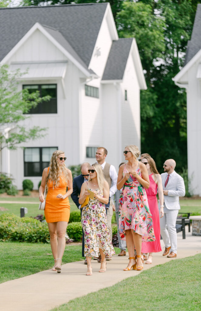wedding guests in colorful bright dresses walking up a concrete path at Bay Pointe Woods