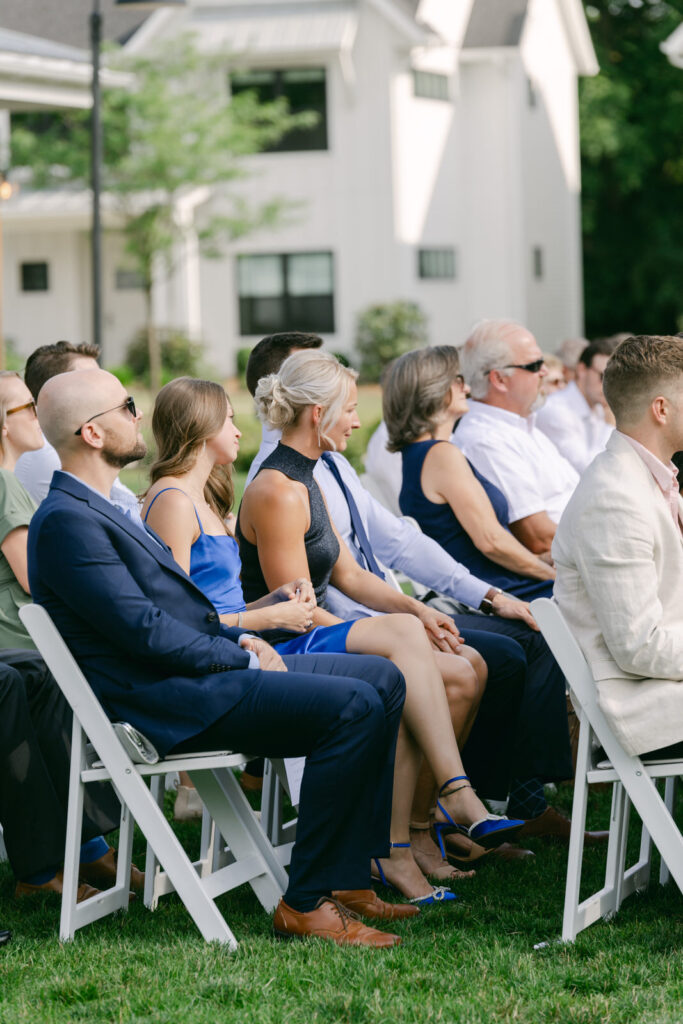 wedding guests sitting in white chairs watching a wedding ceremony at Bay Pointe Woods