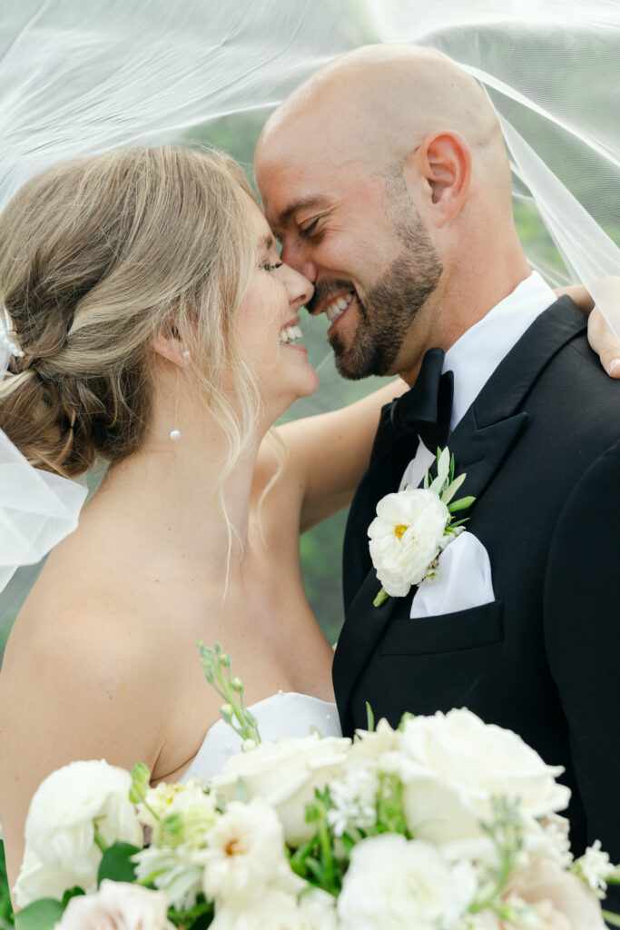 bride and groom touching noses and smiling under the veil on their summer wedding day at Bay Pointe Inn