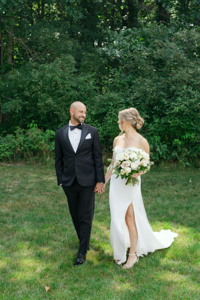 bride and groom holding hands and walking against lush greenery on a sunny summer day