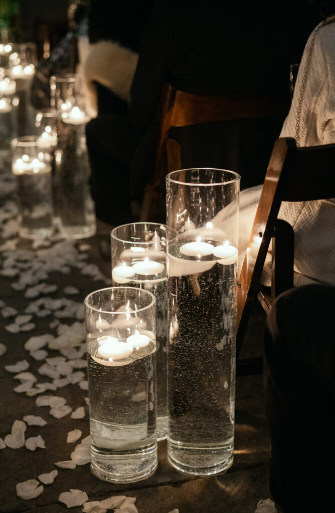 3 large glass vases full of water and floating candles illuminating the wedding ceremony aisle at night