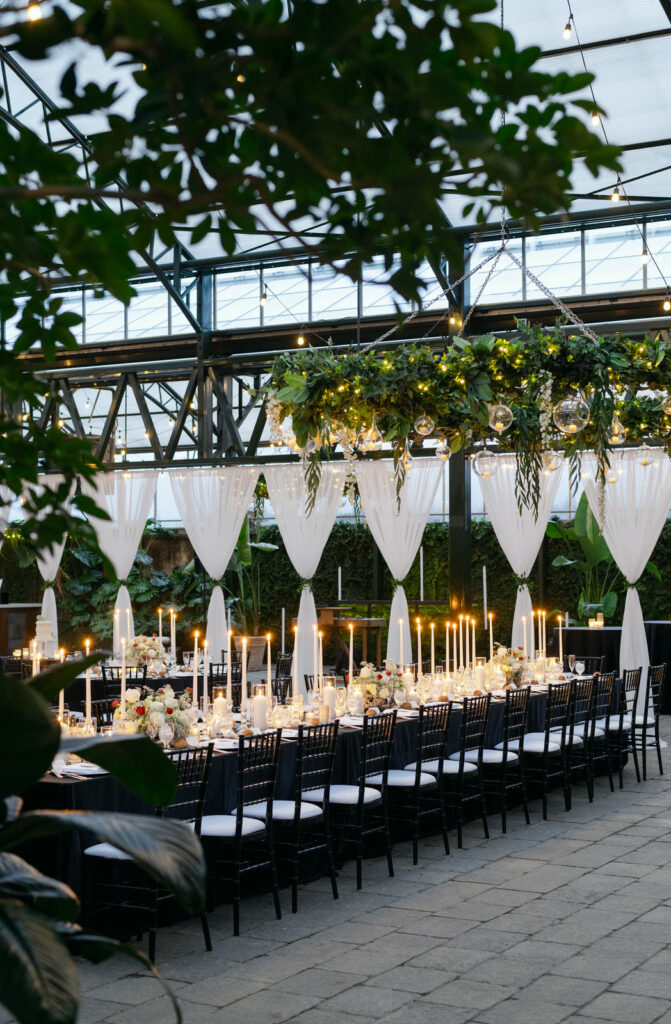 Long reception table with glowing candles, black table cloth, and white floral arrangements at night at Planterra Conservatory