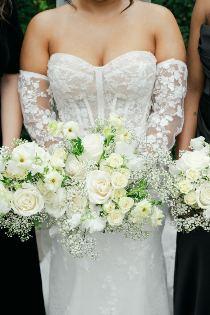 A bride holds her wedding bouquet full of white roses and babys breath