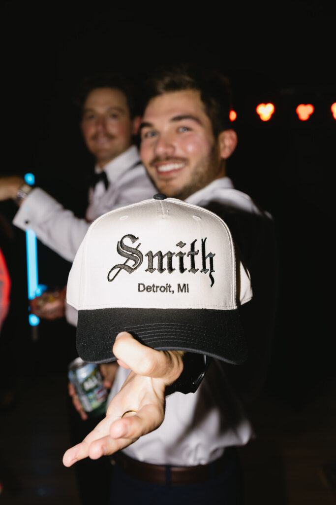 wedding guest holds out a hat on the dance floor that reads "Smith Detroit, MI"