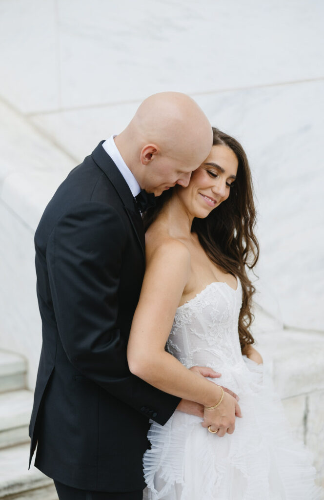 bride rests her back against her groom's chest while they hold hands at the Detroit Institute of Arts