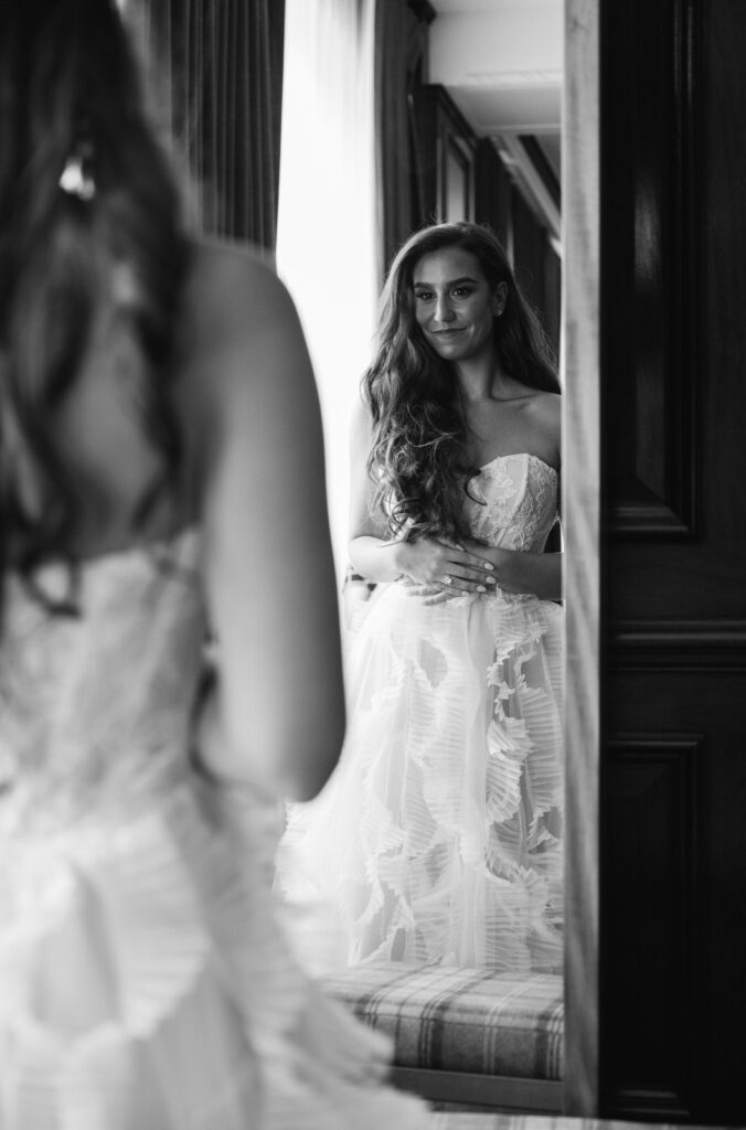 bride looks at herself in her wedding dress in the mirror on her wedding day in Detroit