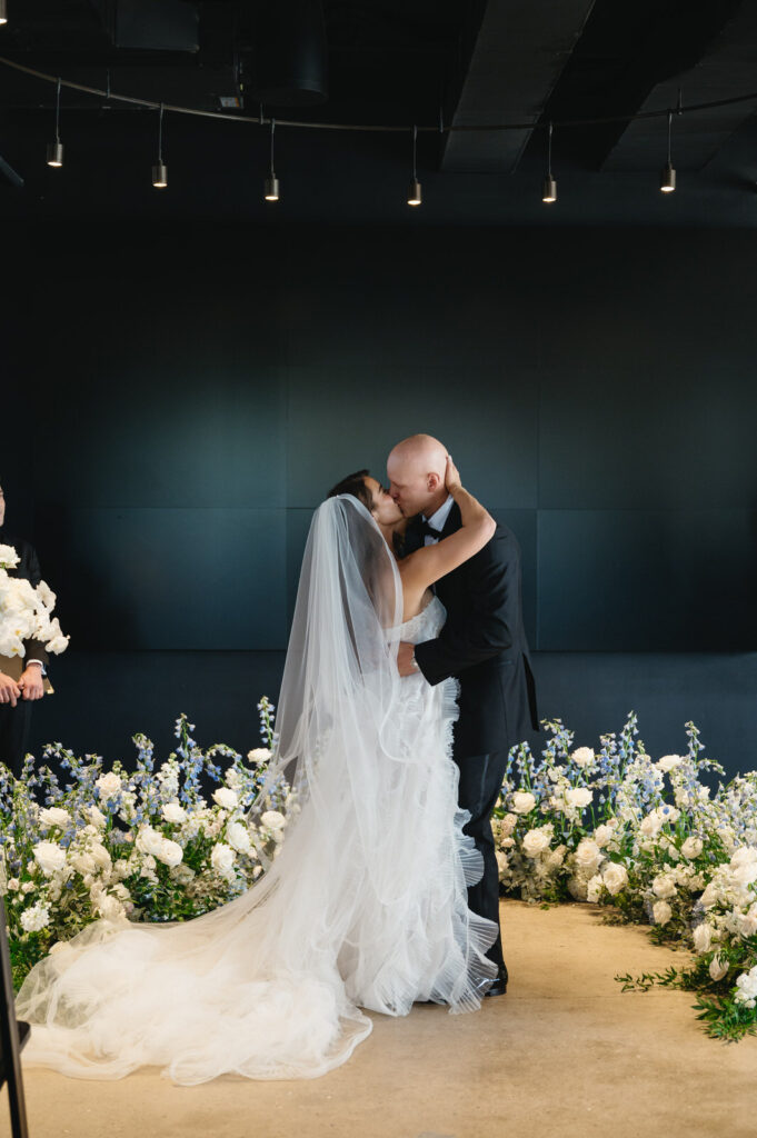 bride and groom share their first kiss as husband and wife surrounded by blue and white flowers during their Chroma Detroit wedding ceremony