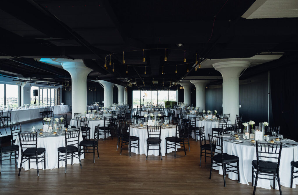 wedding reception decor on the 9th floor of Chroma Detroit featuring black chairs, white table clothes, and single white rose stems