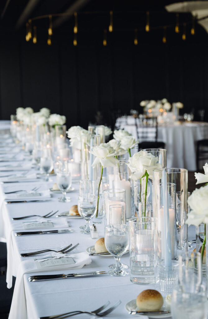 head table of a wedding reception at Chroma Detroit with single white stem roses and light blue candles across the table