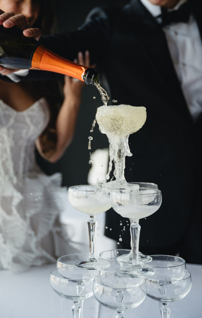 bride and groom pouring champagne into the top glass of their champagne tower