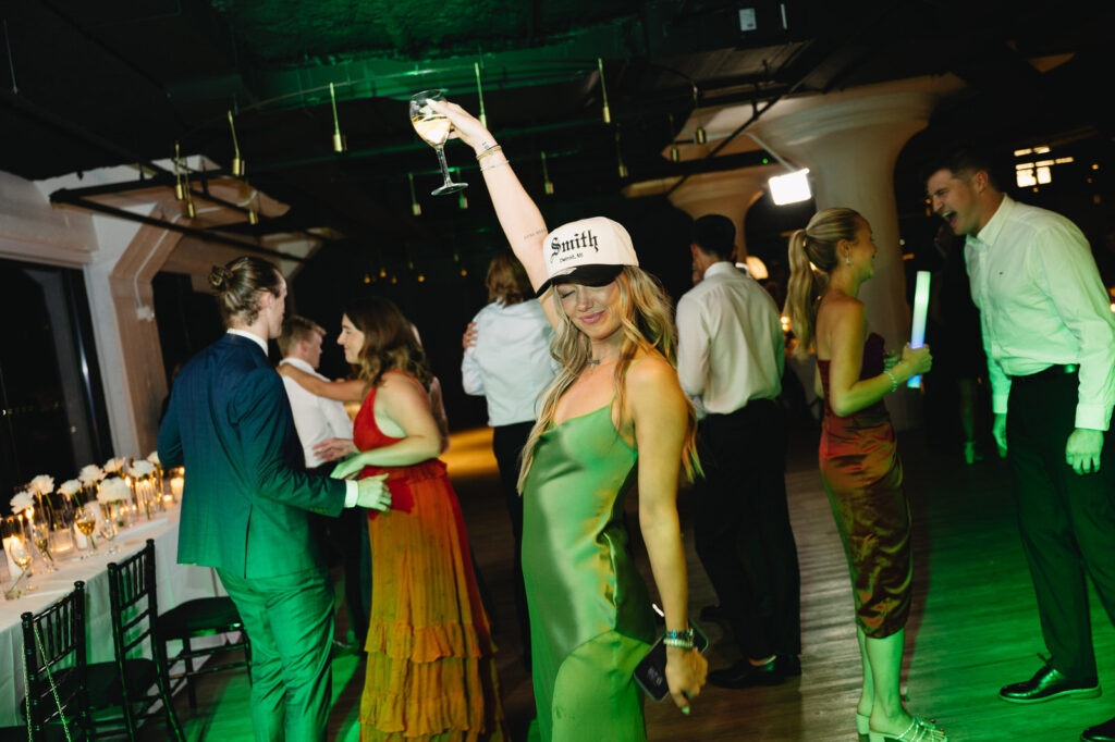 female wedding guest in a green satin dress holds up a drink on the dance floor of Chroma Detroit