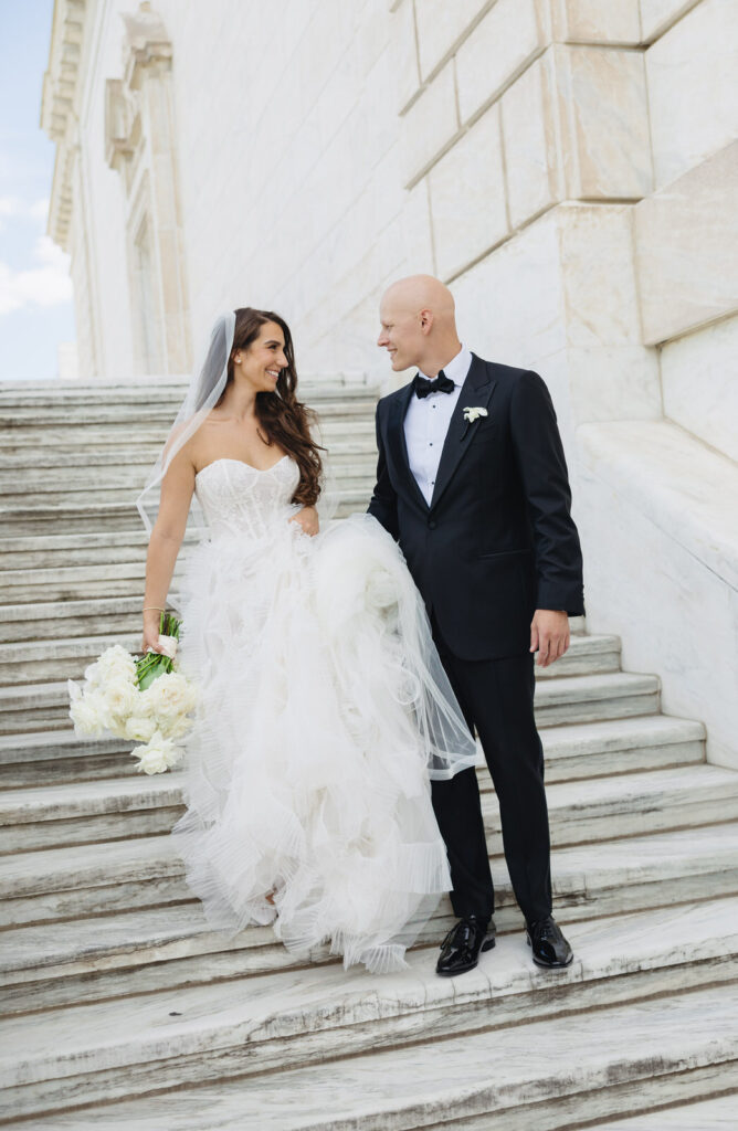 bride in an Ines Di Santo gown and groom in a black suit walk down the marble stairs of the Detroit Institute of Arts