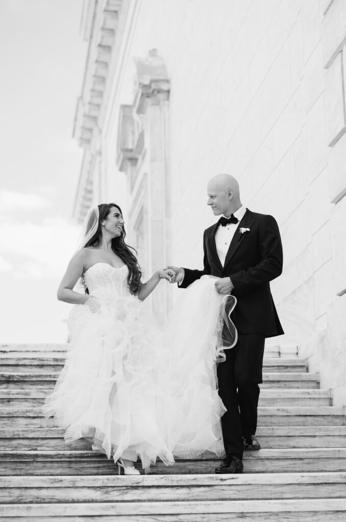 groom guides his bride down the marble steps of the Detroit Institute of Arts on their wedding day