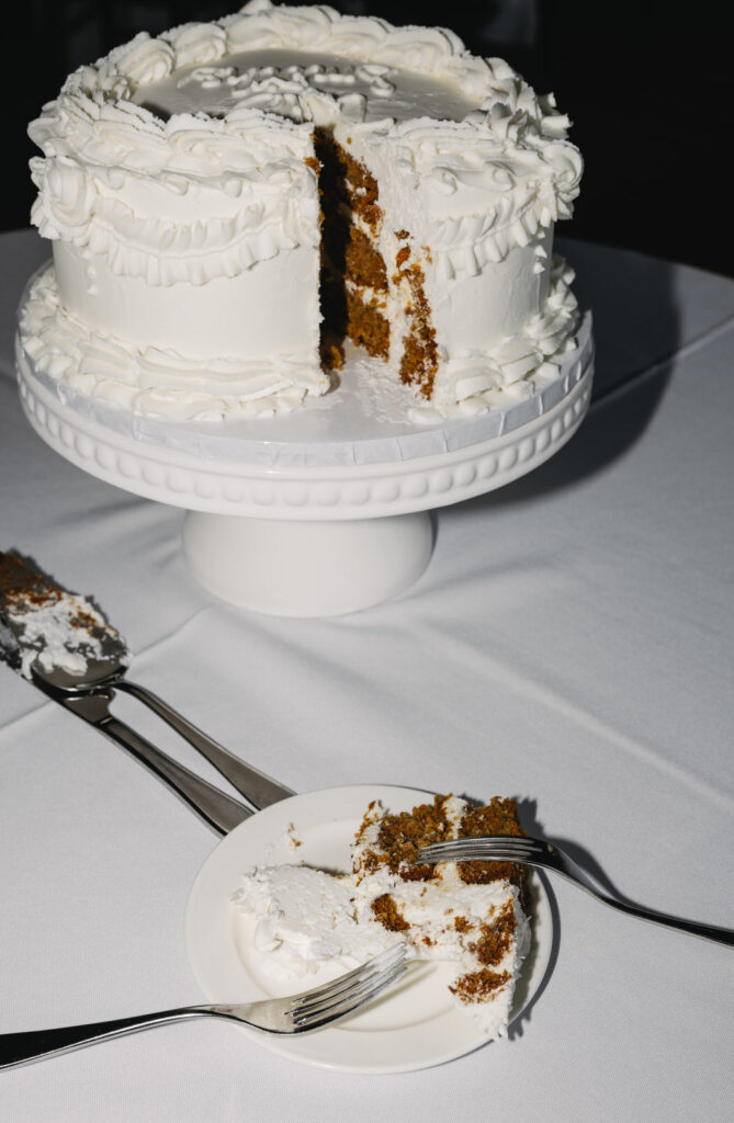 a white cake made by Sweet Bree's Bakeshop in Detroit on a white cake stand with a piece cut and plated with forks