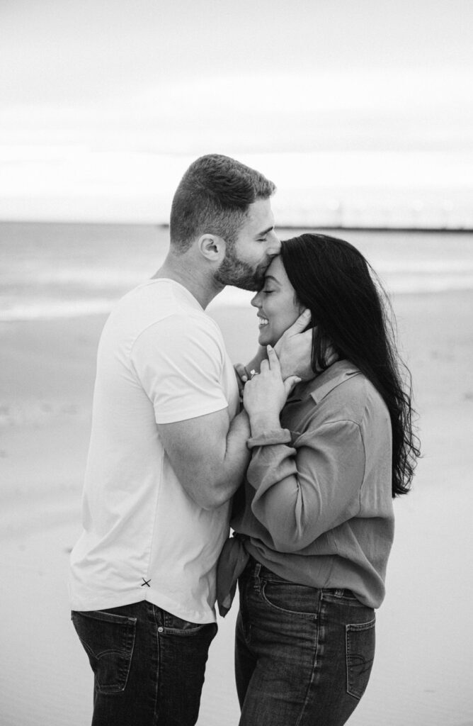 man kissing his fiance's forehead at sunset with the South Haven lighthouse pier in the background