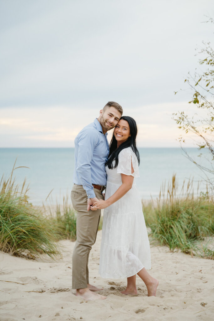 woman in a white dress and man in khakis and a blue dress shirt smile at the camera for their South Haven engagement photo session