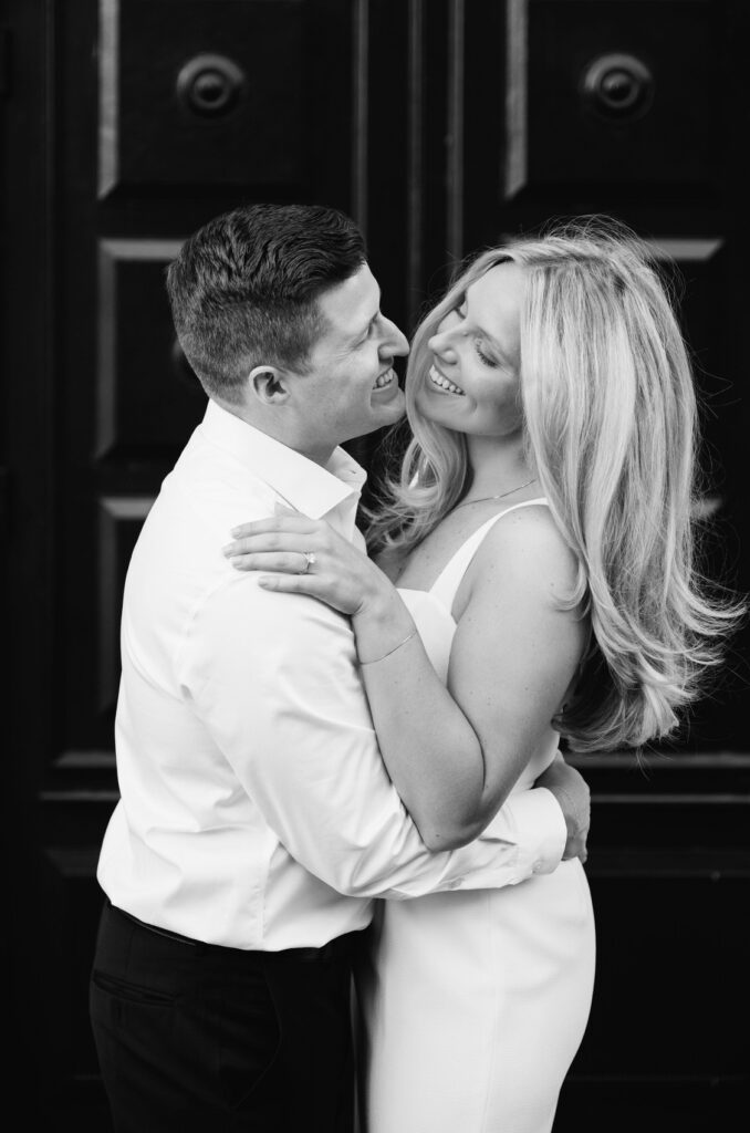 man hugging his fiance and smiling in front of the black door of the Amway Grand Plaza hotel in downtown Grand Rapids