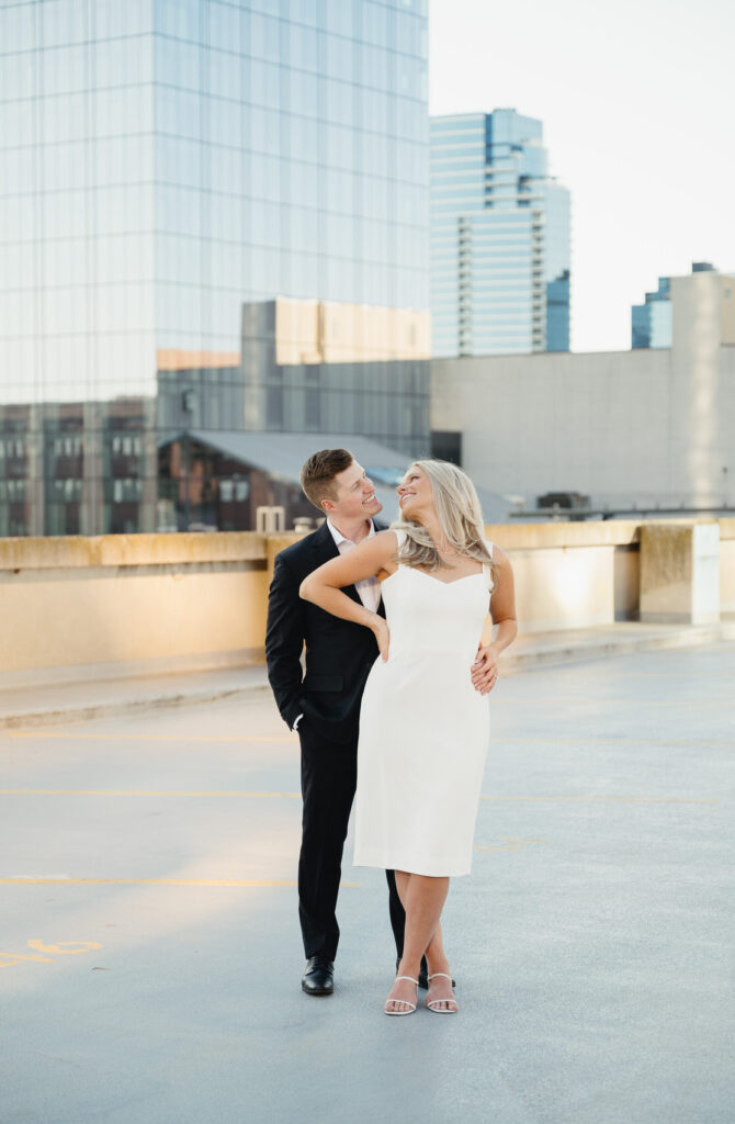 man in a black suite smiling at his fiance in a white dress on top of the Amway Grand Plaza Hotel parking structure