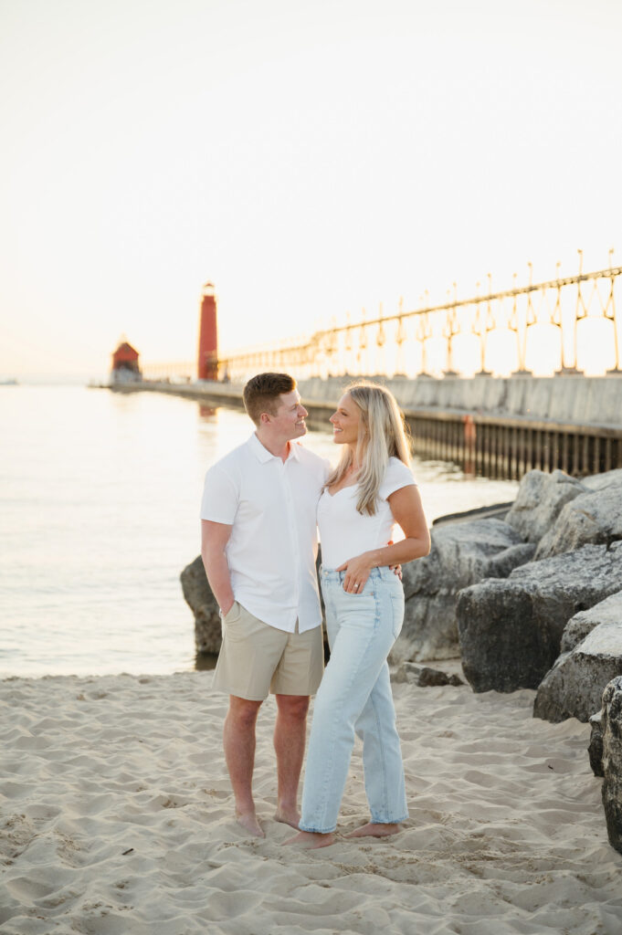 engaged couple smiling at each other at sunset in front of the pier during their west Michigan engagement session