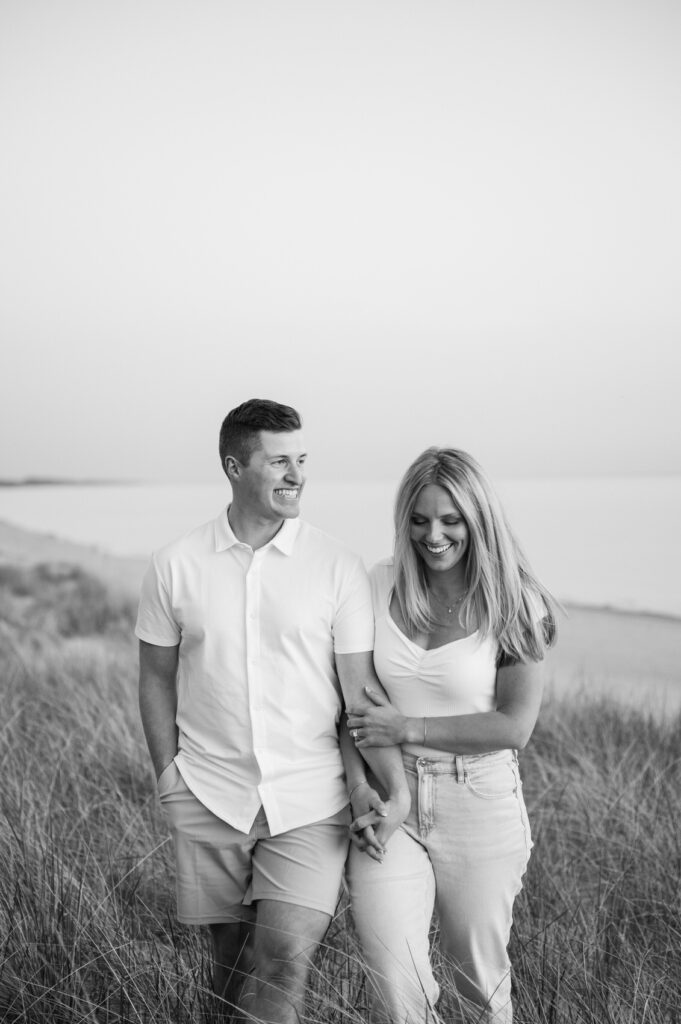 couple walking hand in hand on top of the sand dunes with Lake Michigan behind them at their West Michigan engagement session