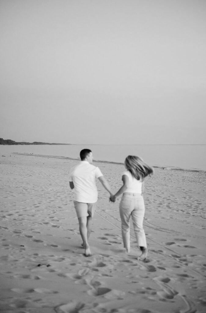 couple running while holding hands toward Lake Michigan during their West Michigan engagement session