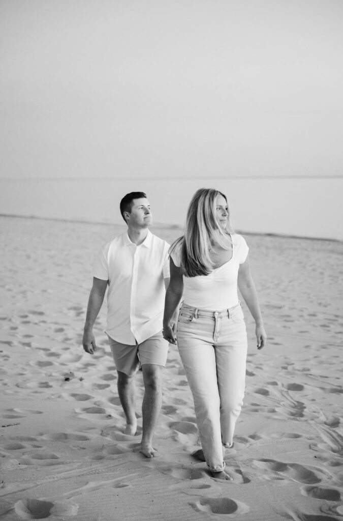 woman holds her fiance's hand as they both look out across the Lake Michigan horizon during their West Michigan engagement session