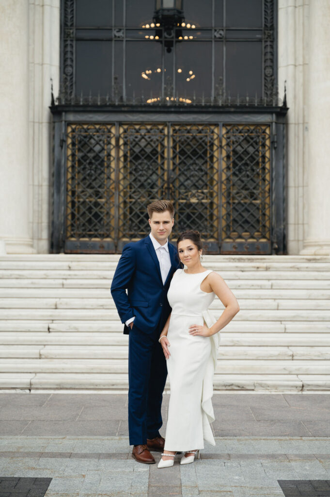 engaged woman in a long white dress and her fiance in a navy blue suit in front of the Detroit Institute of Arts
