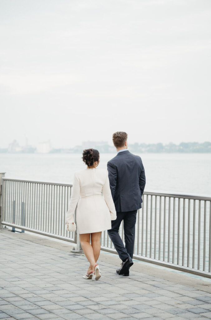 couple walking hand in hand looking towards the Canadian skyline on the Detroit Riverwalk