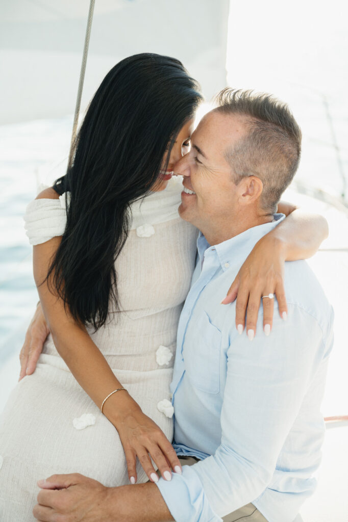 woman sits on her fiance's lap as they both smile during their engagement session