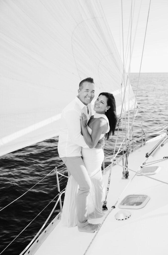 woman snuggles up to her fiance as he hugs her waist on a sailboat
