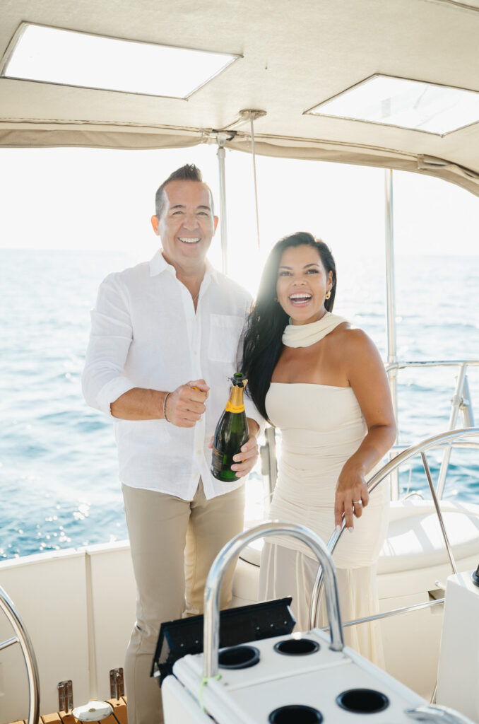 man pops a bottle of Veuve Clicquot on a sailboat sailing on Lake Michigan at sunset